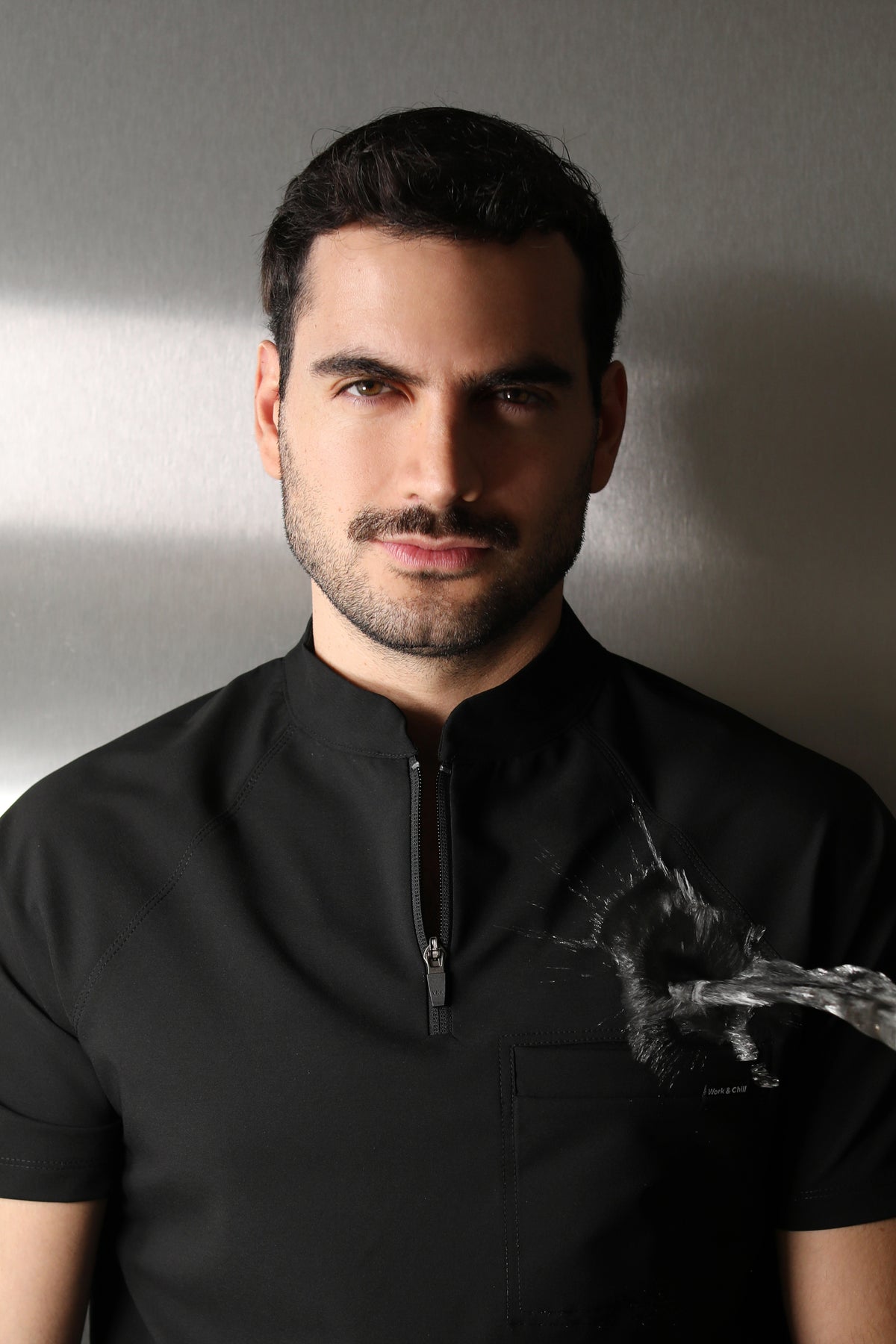 Close-up portrait of a man wearing the Harry Black W&C Shield™ scrub top during a water-repellency demonstration.