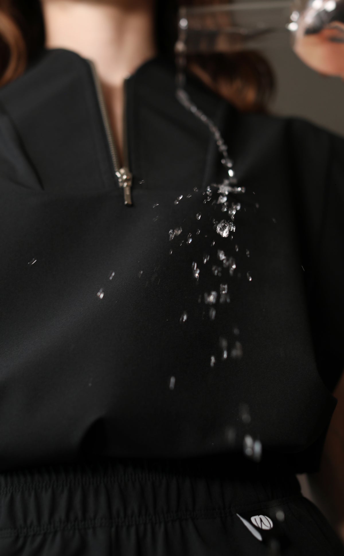 Close-up of clear liquid splashing and beading on the black fabric of the Kate W&C Shield™ scrub top.